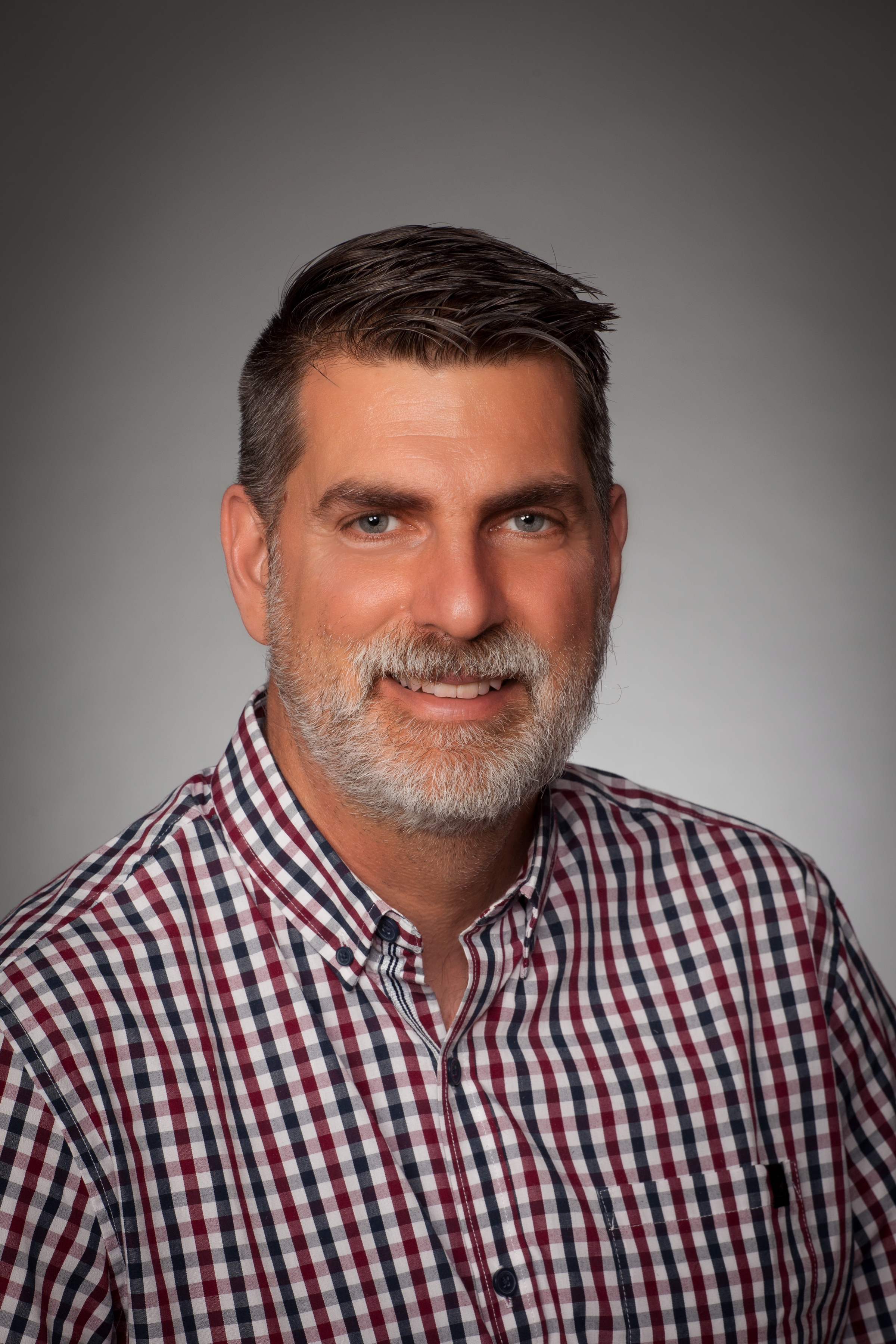 A man with a grey beard and dark hair smiles at the camera. 