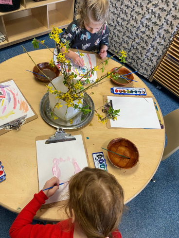 Two children sit at a table and paint. 