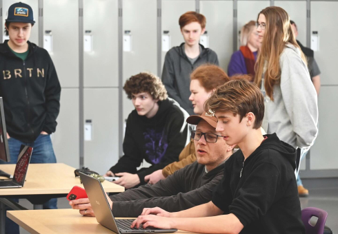 A group of students gather around a computer. 