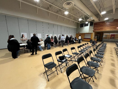 A group of people stand along a wall writing on poster paper. 