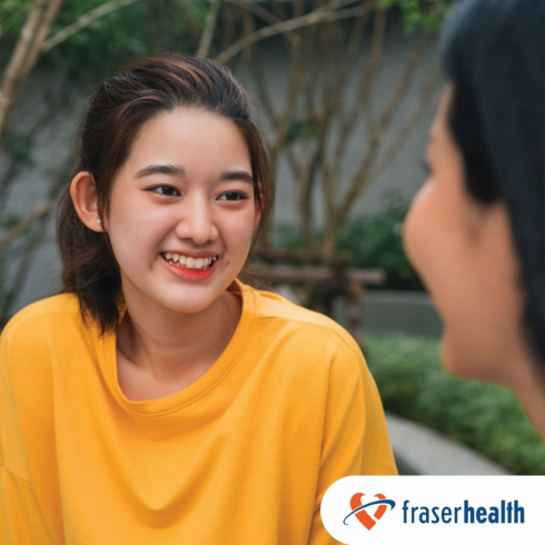 A girl wearing a yellow shirt is smiling as she talks to a peer. 