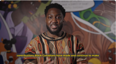 A still from a recorded video of a Black man wearing a sweater with colourful patterns.