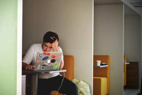 A youth drags a hand through their hair. They are looking at a laptop. 
