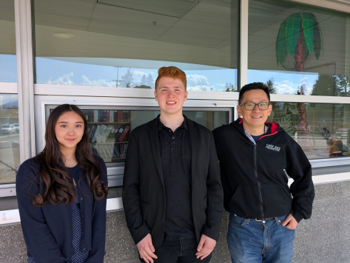 Two youth and an adult stand in front of a row of windows. They are smiling. 