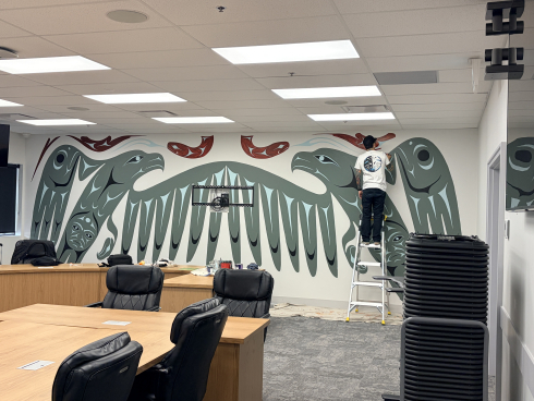 A person in a white shirt stands on a ladder and paints a mural. 