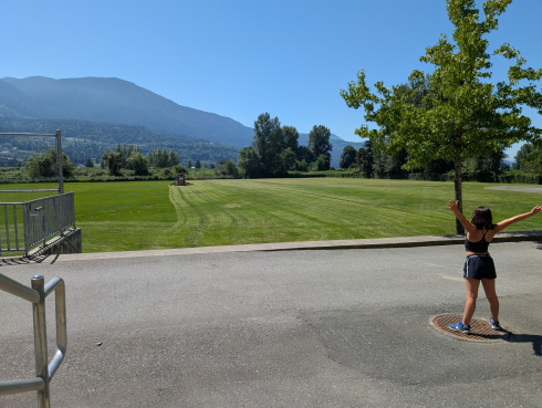 A child with outstretched arms looks towards a school field on a sunny day. 
