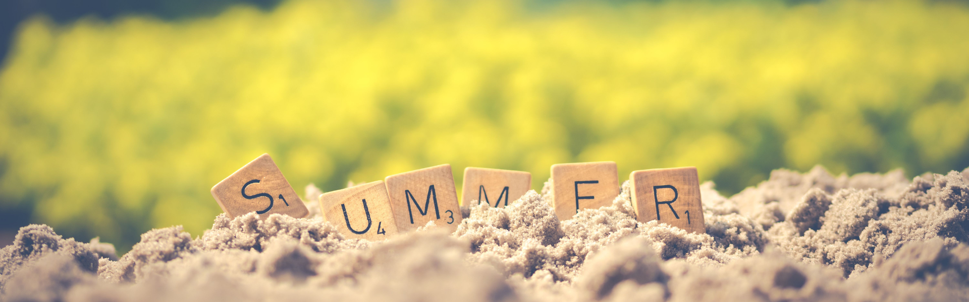 Scrabble tiles in a pile of sand spell out the word summer