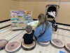 An adult and a child sit on cushions and read a book together. 