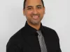 A man with a black button up shirt and tie. He is smiling. 