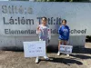 Two students stand in front of their school sign. They have signs about the importance of diversity. 