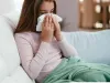 A girl on a couch uses a tissue. 